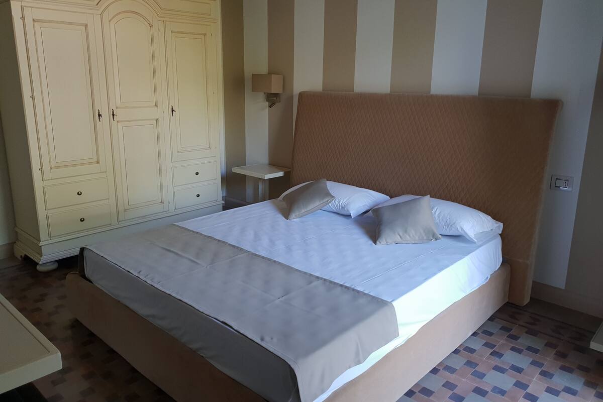 A bedroom with a large bed, a wardrobe, a bedside table, and a wall-mounted lamp.