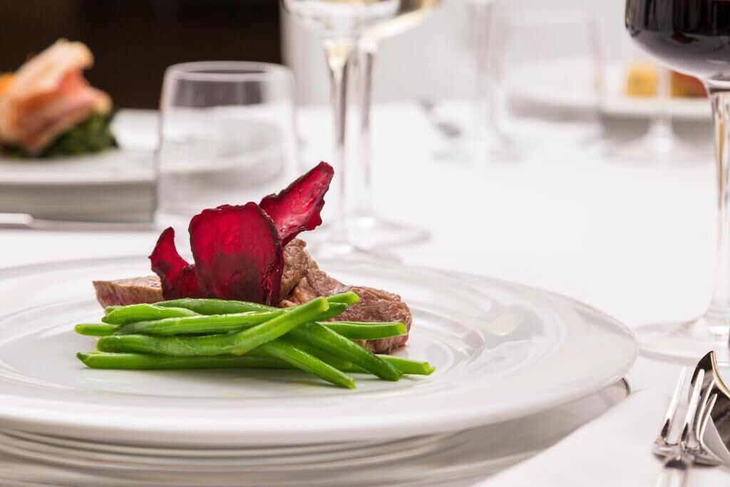 Une assiette blanche avec des haricots verts et une fleur rouge, un verre de vin blanc et une fourchette sur une table.