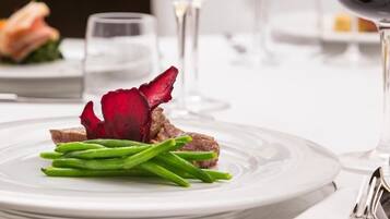 Une assiette blanche avec des haricots verts et une fleur rouge, un verre de vin blanc et une fourchette sur une table.