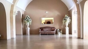 Un vaste hall doté d’un haut plafond en arc de cercle, d’un canapé central et de deux grands vases remplis de fleurs.