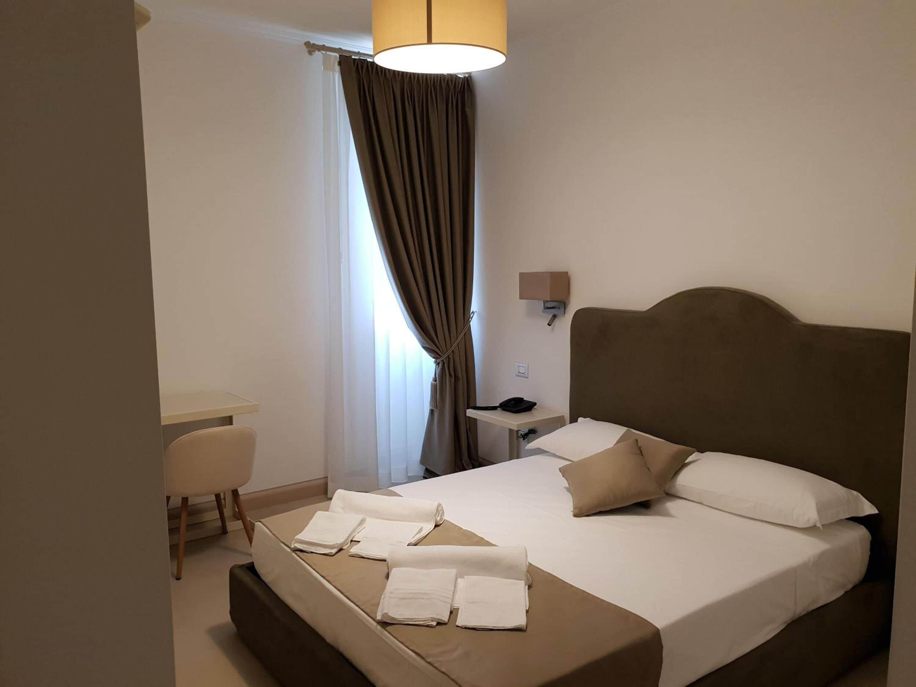Een hotelkamer met een bed, nachtkastje, lamp en een bureau met stoel.