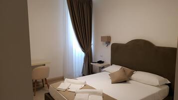 Een hotelkamer met een bed, nachtkastje, lamp en een bureau met stoel.