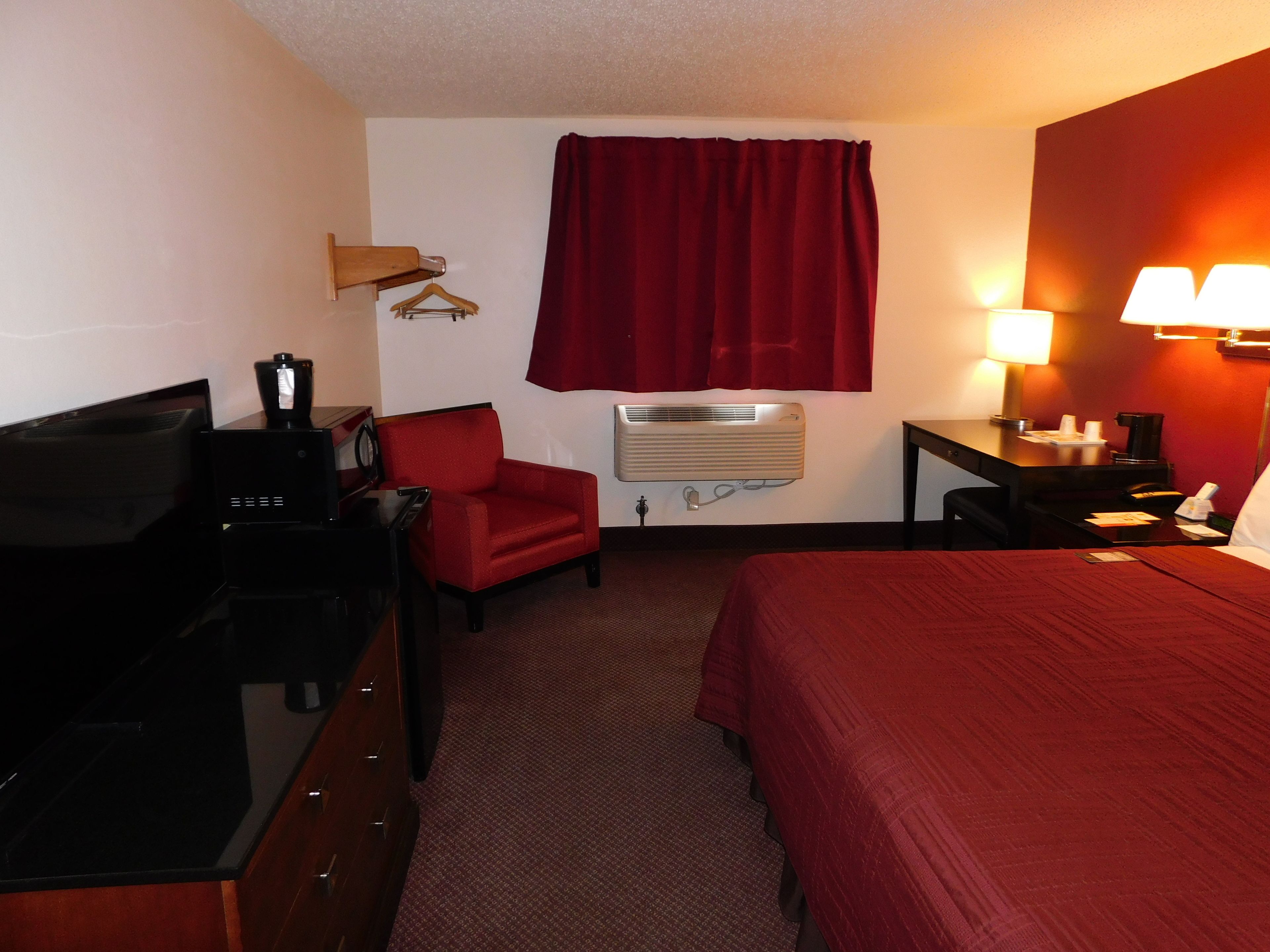 Habitación de hotel con cama, escritorio, silla, televisor, calefactor y ventana con cortinas.