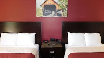 Habitación de hotel con dos camas, cabecera de madera, pared roja y un cuadro de un puente cubierto.