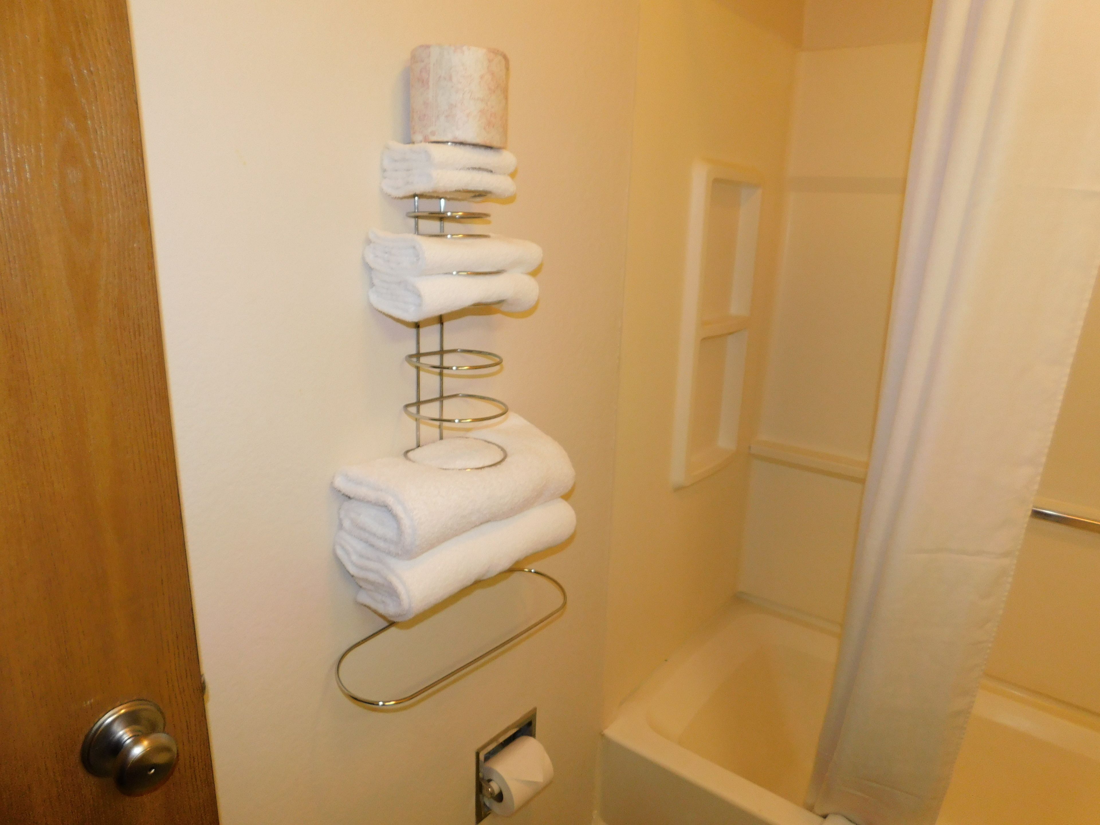 A bathroom with a towel rack holding several folded towels, a toilet paper holder, and a shower curtain.