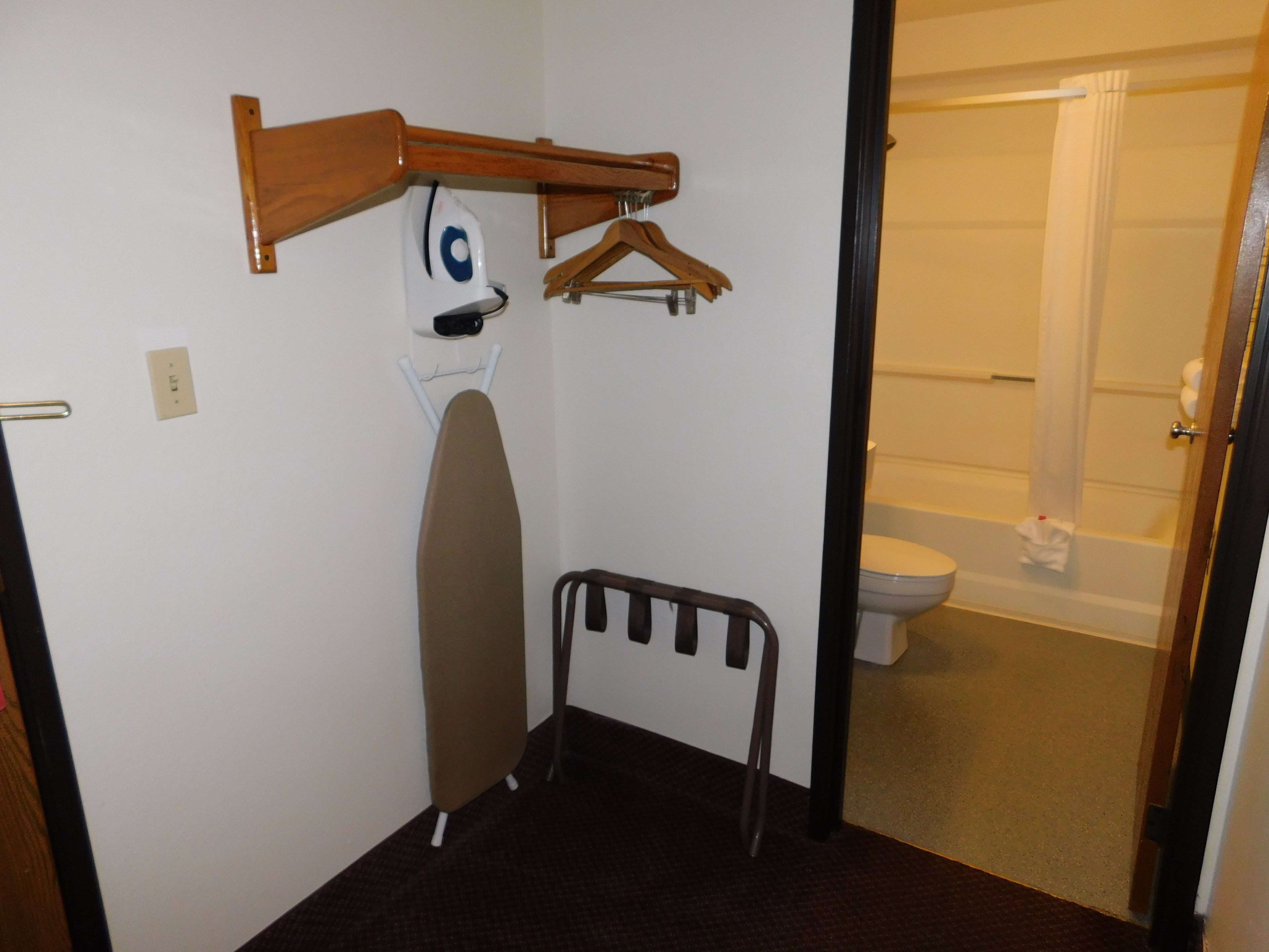 A small room with a wooden ironing board, a hanging clothes rack, and a white wall.