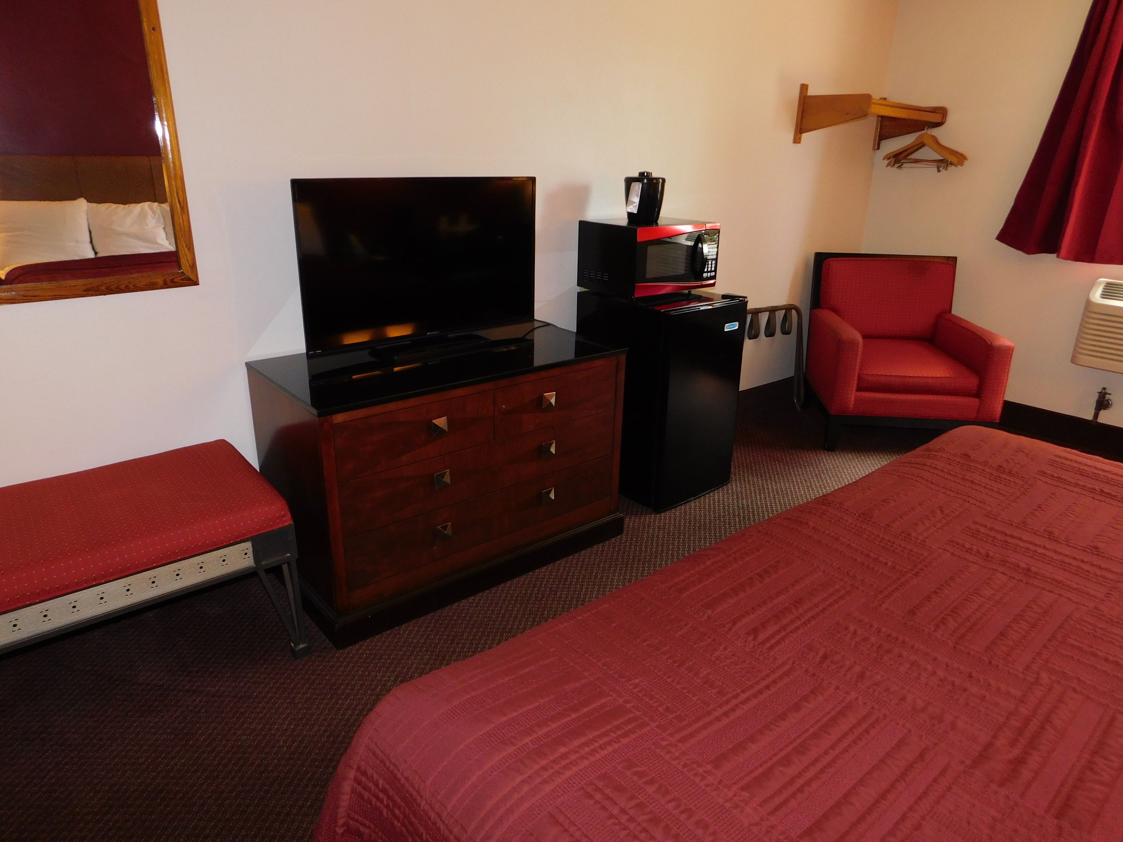 Ein Hotelzimmer mit Fernseher, Minibar, einem roten Sessel und einem Bett.