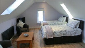 Un dormitorio con techo inclinado, dos camas, una mesita, una silla y un ventanal.