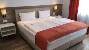 A double bed with a white and red blanket, two white pillows, a wooden headboard, bedside tables with lamps, and a red curtain. - Pension Haus Erika (Stadtprozelten)