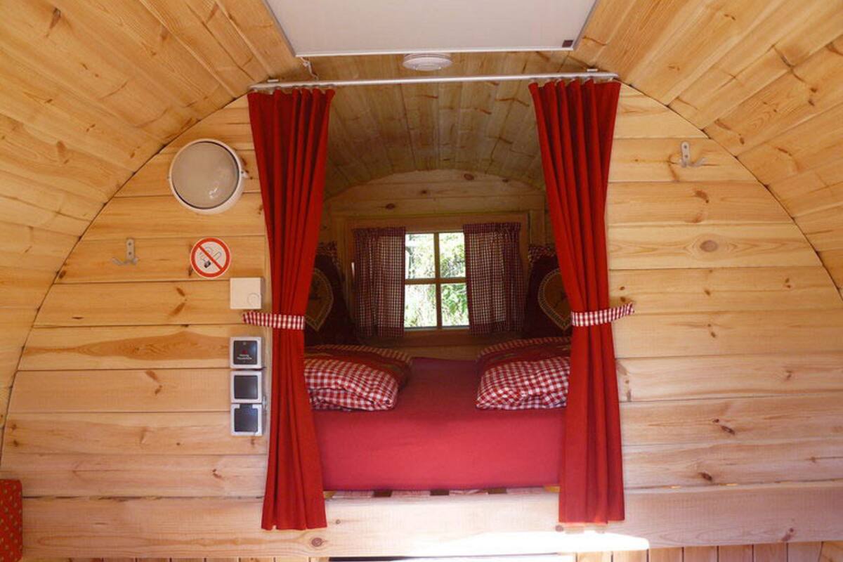 Une cabane chaleureuse avec un lit en mezzanine, des rideaux rouges et une fenêtre ornée de rideaux à carreaux.