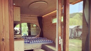 A compact RV interior with a bed, a small kitchenette, and a large window. - Camping Schwabenmühle (Weikersheim)