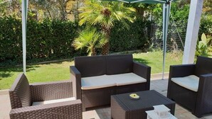 An outdoor seating area with wicker furniture, including a sofa and chairs, under a green canopy. - B&B Santa Maria Apparente (Civitanova Marche)