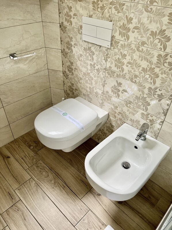 A bathroom with a toilet and bidet, tiled walls, and wooden flooring. - B&B Santa Maria Apparente (Civitanova Marche)
