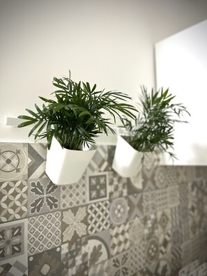 Two potted plants on a white shelf against a tiled wall with geometric patterns.