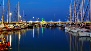 A marina at dusk with numerous sailboats docked, a bridge in the background, and calm water reflecting the lights. - B&B Santa Maria Apparente (Civitanova Marche)