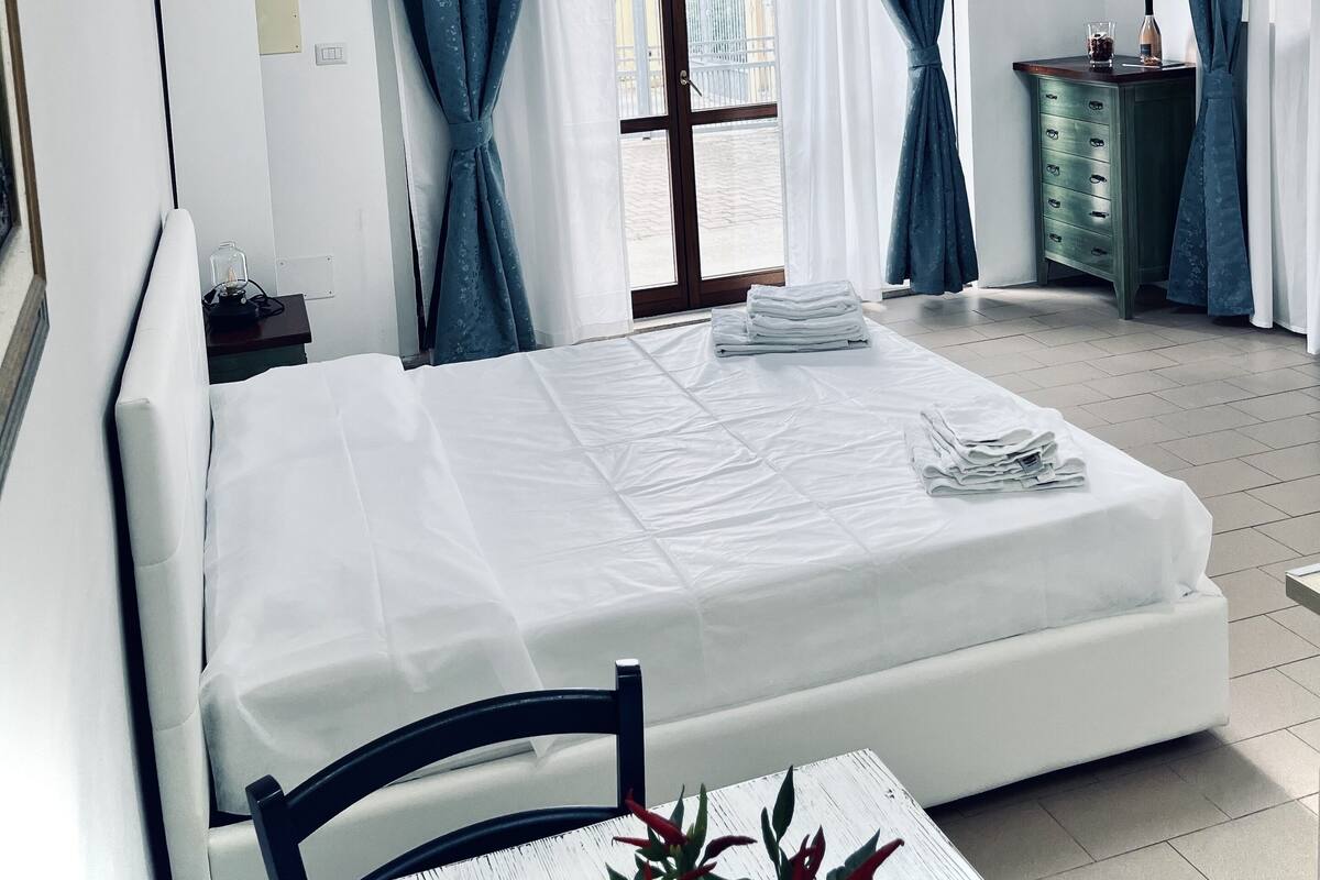 A hotel room with a bed, a chair, a table, a dresser, and a window with curtains.