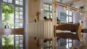 A room with large windows, wooden furniture, and a view of greenery outside. - Hostel La Maison Montreau (Montreuil)