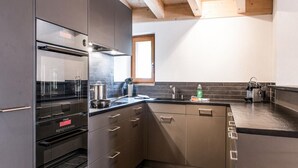 A compact kitchen with built-in appliances, a window, and a wooden ceiling. - Titlis Resort (Engelberg)