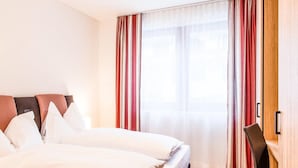 A hotel room with a bed, a desk, and a window with curtains. - Titlis Resort (Engelberg)
