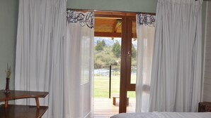 Une chambre avec un lit en bois, un bureau en bois et une vue sur une terrasse et un espace extérieur, visible à travers une porte vitrée.