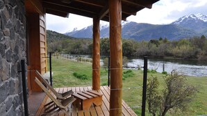 Une terrasse en bois avec un banc, offrant une vue sur une rivière et des montagnes.