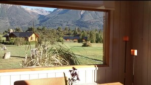 Une pièce dotée d’une grande fenêtre donnant sur un paysage montagneux, avec une table en bois et une bougie posée sur une table de chevet.