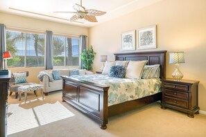 Une chambre à coucher avec un grand lit, une table de chevet, une commode, une chaise, un bureau et un ventilateur de plafond.