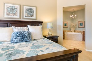 A bedroom with a large bed, a nightstand, a lamp, and a framed floral artwork above the bed.