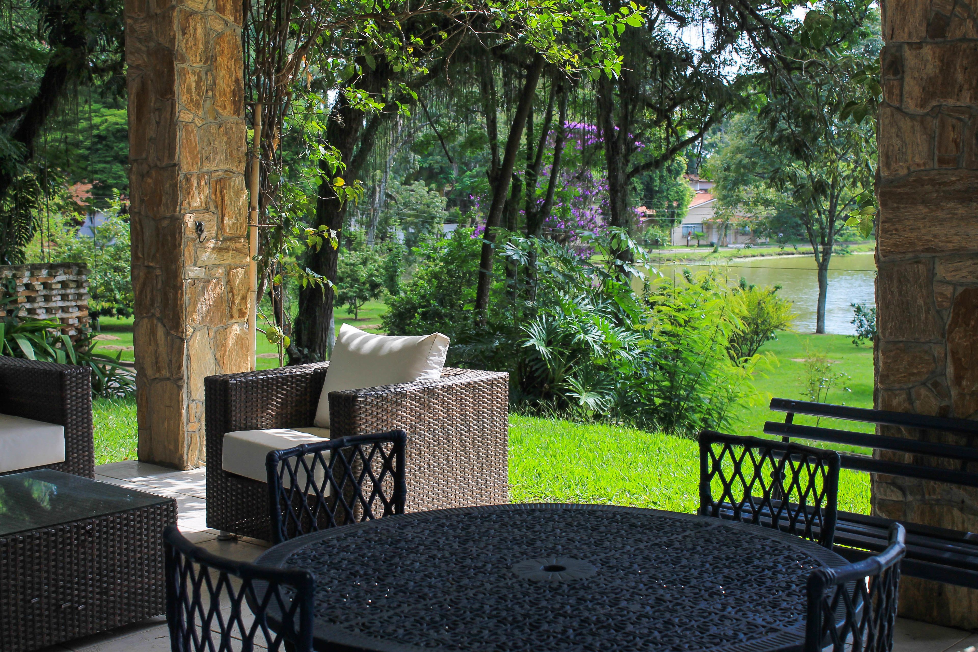 Un patio con mobiliario de mimbre, una mesa redonda y vista a un lago y follaje.