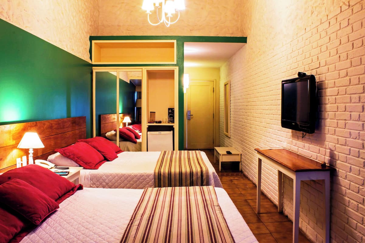 A hotel room with two beds, a television, a desk, and a mirror.