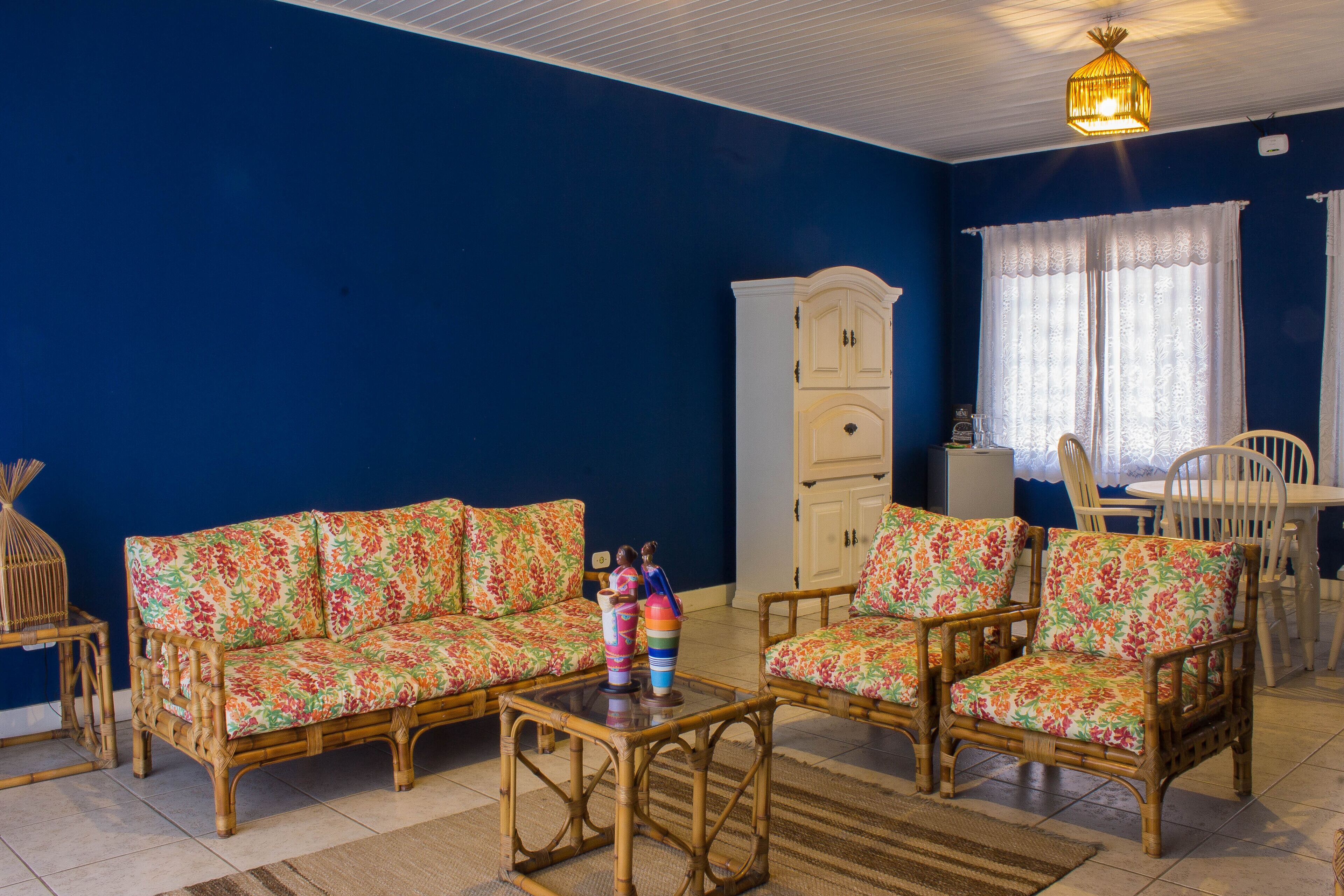 Una sala de estar con pared azul, un mueble blanco, un sofá de mimbre, una mesa de centro de madera y una mesa de comedor con sillas.