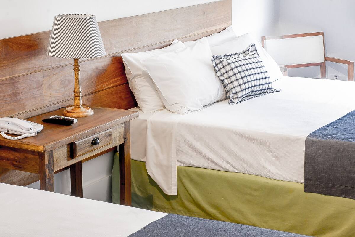 A neatly made bed with white and green bedding, a wooden nightstand with a lamp, and a telephone.