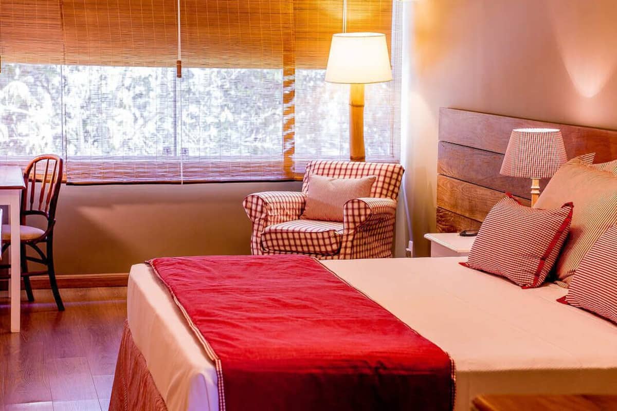 A hotel room with a bed, a chair, a desk, and a window with blinds.