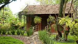A rustic building with a tiled roof, surrounded by lush greenery and a stone pathway leading to the entrance.