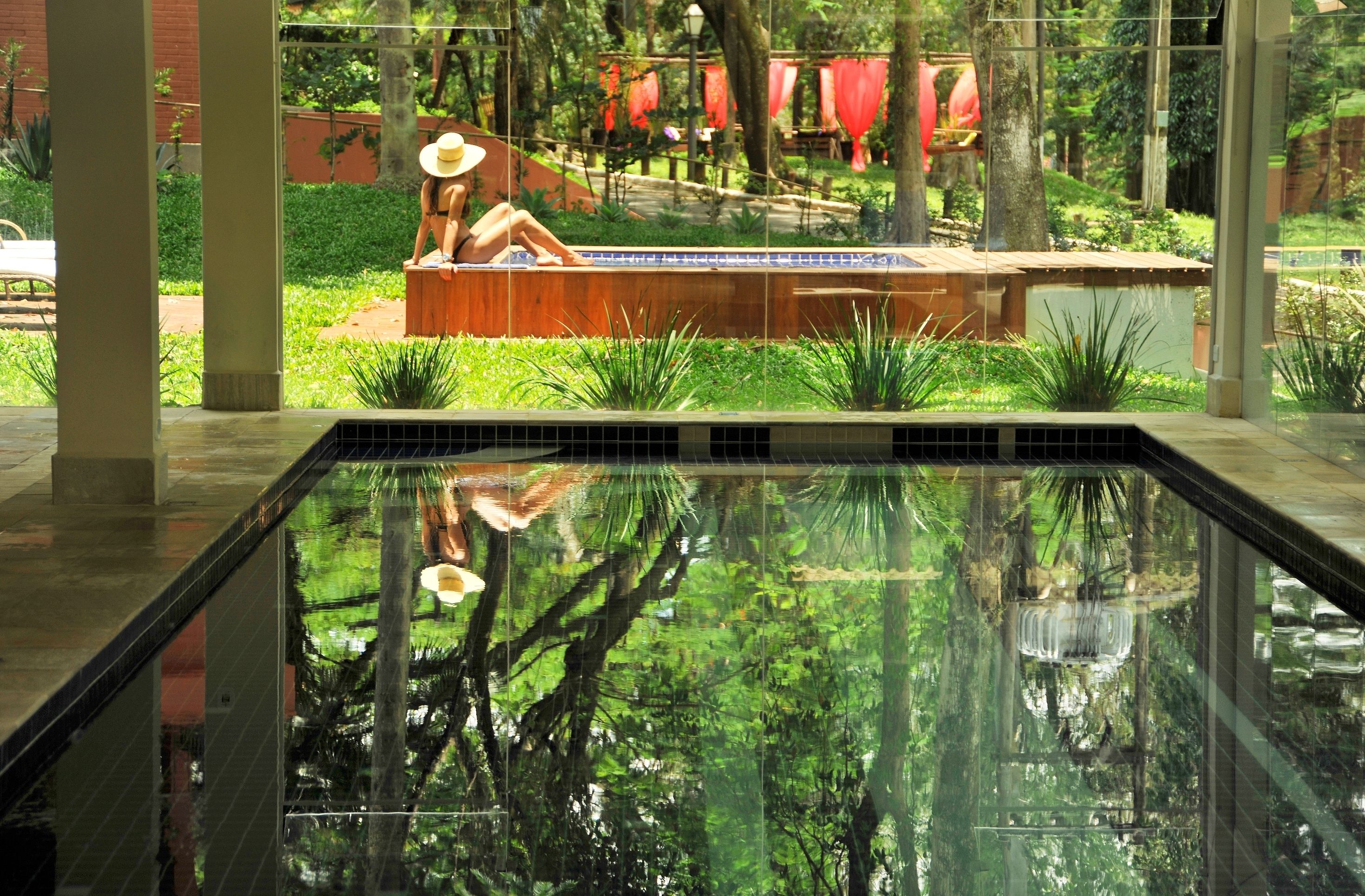 A swimming pool with a reflection of trees and a person sitting on a bench.