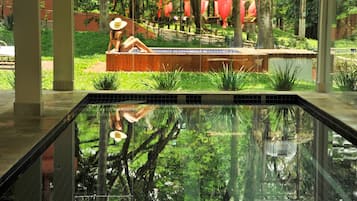 A swimming pool with a reflection of trees and a person sitting on a bench.
