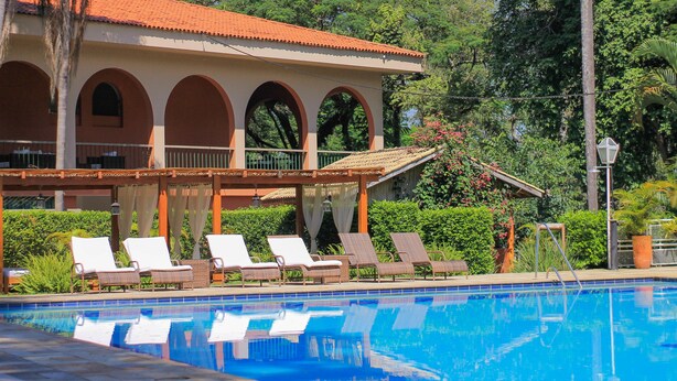 A pool area with lounge chairs, a building with arches, and lush greenery.