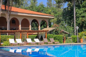 Ein Poolbereich mit Liegestühlen, ein Gebäude mit Bögen und üppigem Grün.