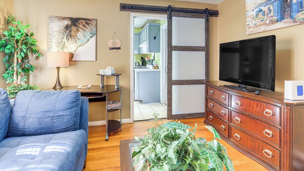 A living room with a sofa, a coffee table with plants, a TV on a wooden cabinet, and a painting on the wall. - 5 Mi to Dtwn ATL! Family Home w/ Veranda & Yard (Atlanta)