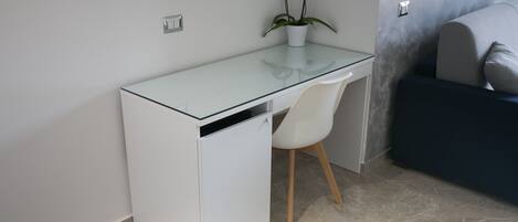 A compact workspace with a glass-top desk, a white chair, and a small potted plant.