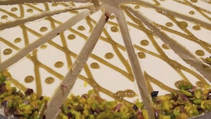 A round cake with white icing and gold drizzle, garnished with chopped nuts. - Tropea Luxury & Charm (Tropea)
