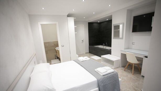 A modern hotel room with a large bed, a desk, a chair, a TV, a bathtub, and a shower. - Tropea Luxury & Charm (Tropea)