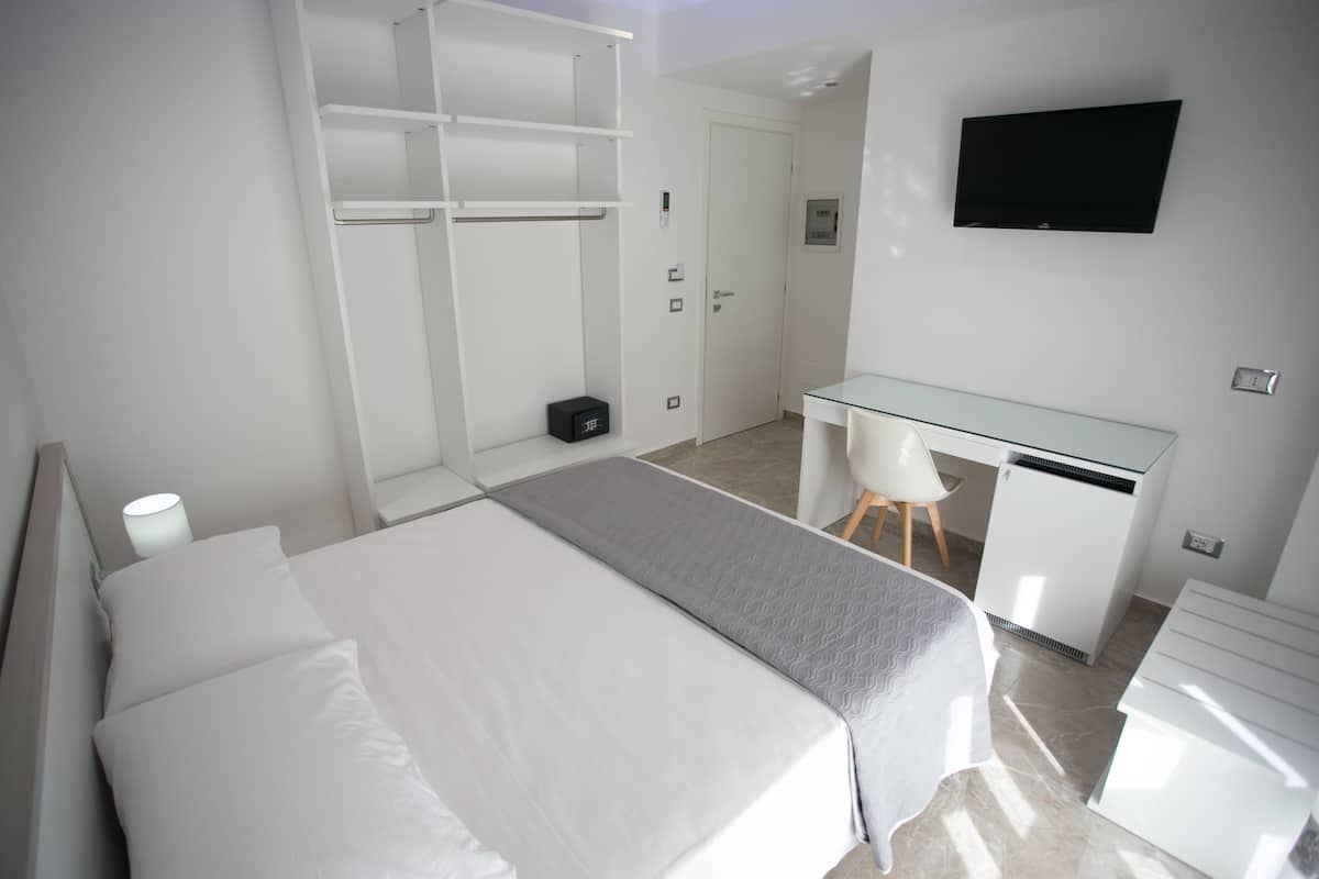 A modern bedroom with a bed, a desk, and a TV.