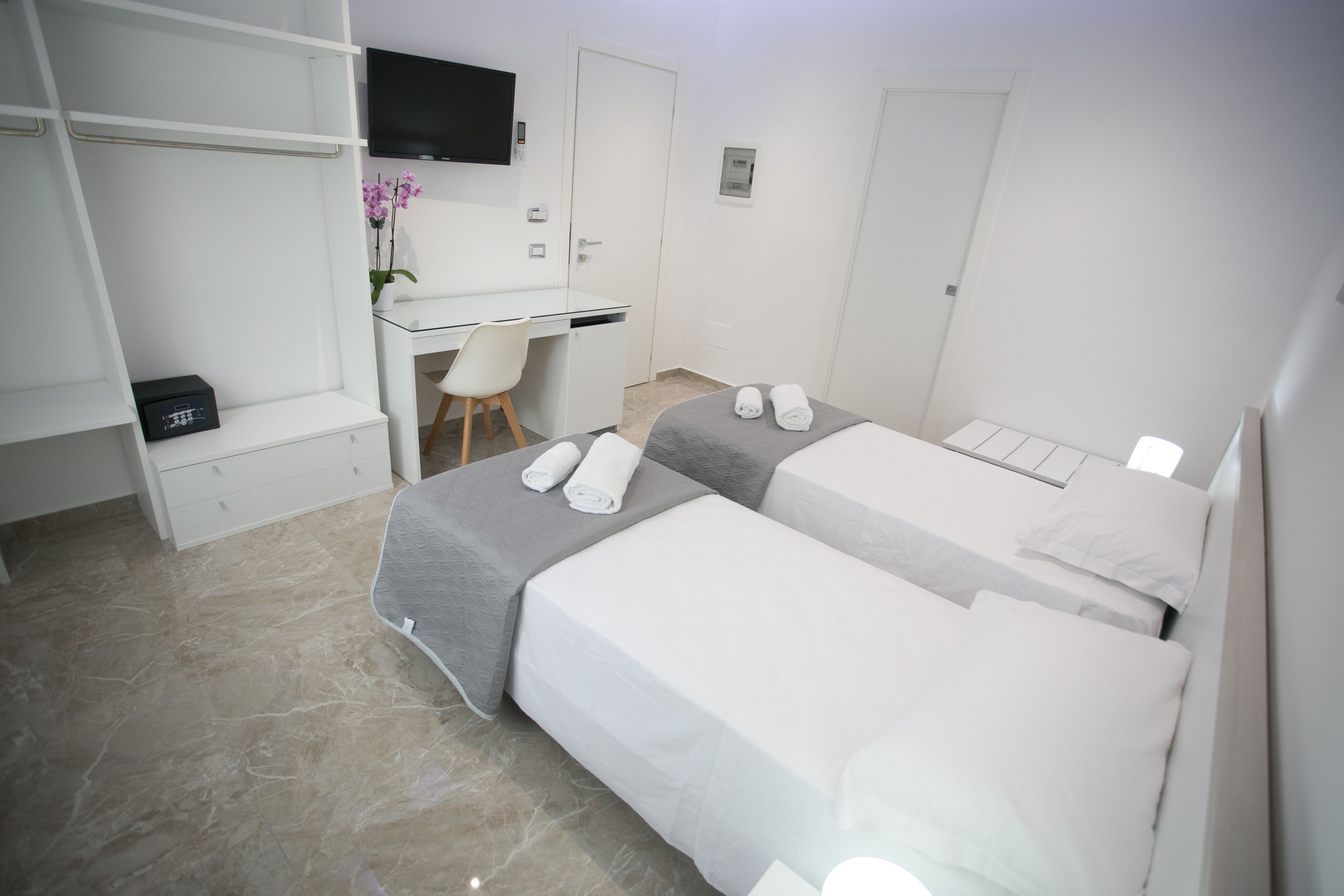 A hotel room with two beds, a desk, a chair, and a TV.