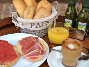 Un esmorzar preparat amb pa, pernil, suc d'aranja i una beguda de cafè damunt d'una taula.