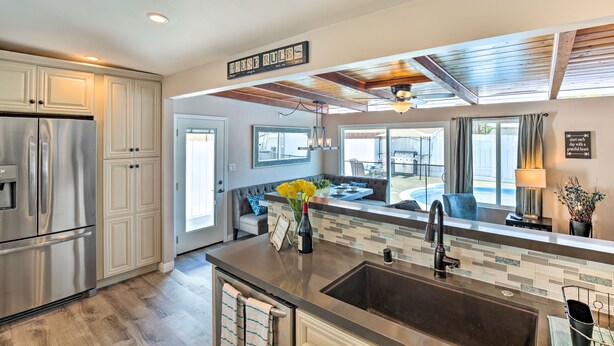 A modern kitchen with a stainless steel refrigerator, a large island with a sink, and a dining area visible through the window. - Chic Central San Diego House w/ Private Pool! (San Diego)