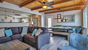 A spacious living area with a large sectional sofa, a wooden coffee table, and a dining table with chairs. A ceiling fan and pendant lights are visible. - Chic Central San Diego House w/ Private Pool! (San Diego)
