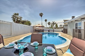 Un patio trasero con piscina, mobiliario exterior y palmeras.