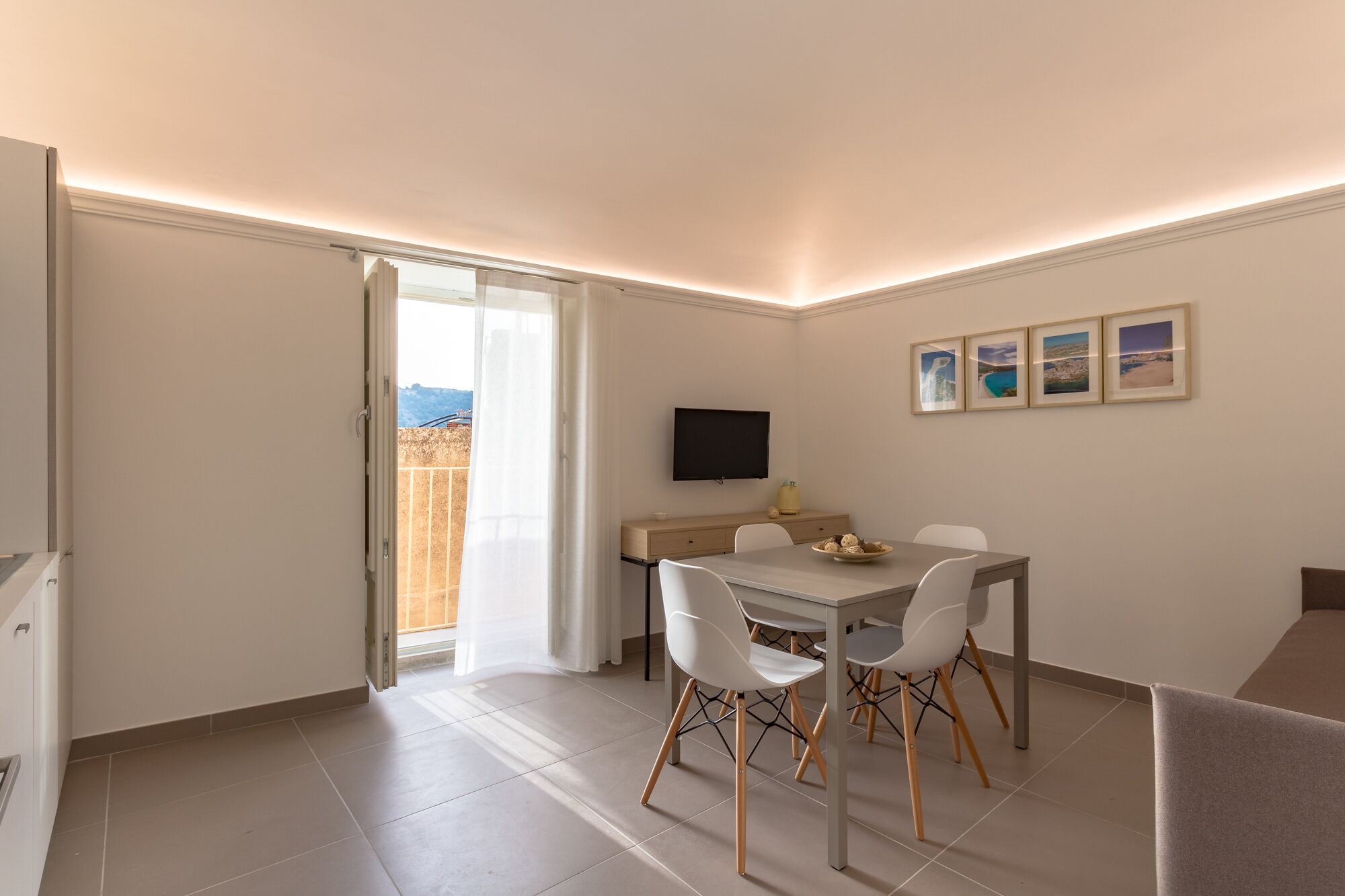 A modern room with a dining table, chairs, a TV, and a balcony with a view.