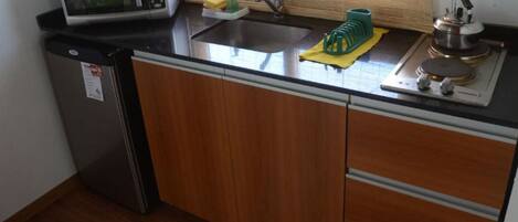 Una cocina compacta con microondas, lavabo y hervidor sobre la encimera.